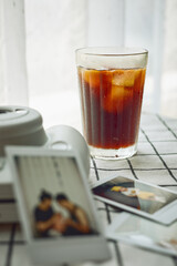 A cold brew coffee with ice on the check cloth table with instant camera and some photos taken