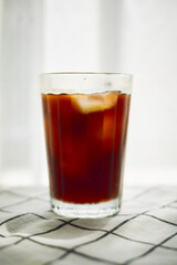 Cold brew cofee with ice on checked cloth beside a window with white curtain