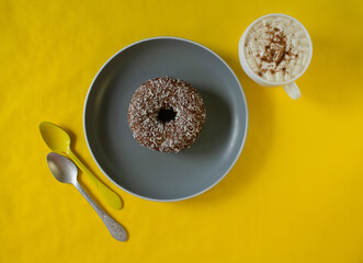 yellow background. a white cup, a gray plate with a donut, spoons.