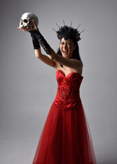portrait of beautiful young asian woman wearing red corset and crown, posing in gothic horror style with creative hand gestures isolated against dark black studio background.