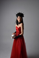 Fototapeta premium portrait of beautiful young asian woman wearing red corset and crown, posing in gothic horror style with creative hand gestures isolated against dark black studio background.