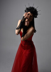 portrait of beautiful young asian woman wearing red corset and crown, posing in gothic horror style with creative hand gestures isolated against dark black studio background.