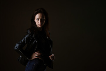 Fototapeta na wymiar portrait of an attractive young brunette woman in a black leather jacket standing on a black background