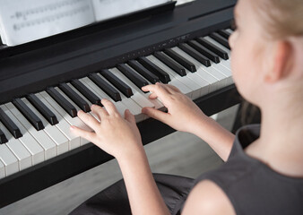 Fototapeta premium a girl in a gray dress plays an electronic piano on a music book . Home Schooling Close up