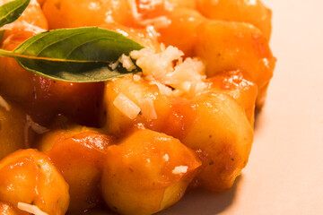 Gnocchi with juice sauce with grated cheese and basil served on the plate. Close-up. Low light. Selective focus.