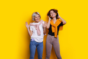 Fototapeta premium Yellow backdrop. Internet technology. Studio room. Dancing studio. Sisters listening to music