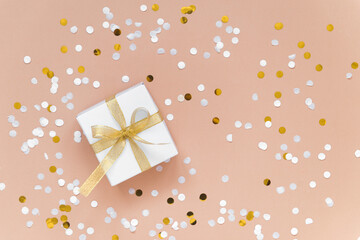 Fototapeta na wymiar white box with ribbon - christmas gift with confetti flat lay on beige background
