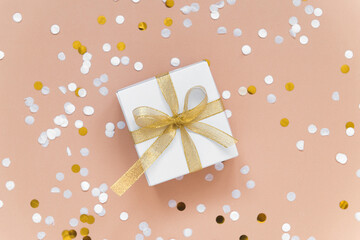 white box with ribbon - christmas gift with confetti flat lay on beige background