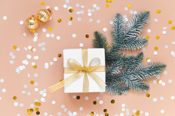 white box for christmas or new year gift on beige background with confetti, gold color balls and fir tree branches