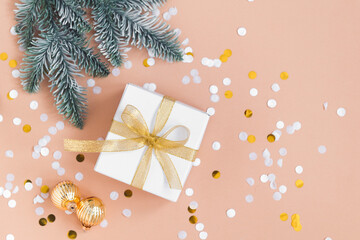 white box for christmas or new year gift on beige background with confetti, gold color balls and fir tree branches