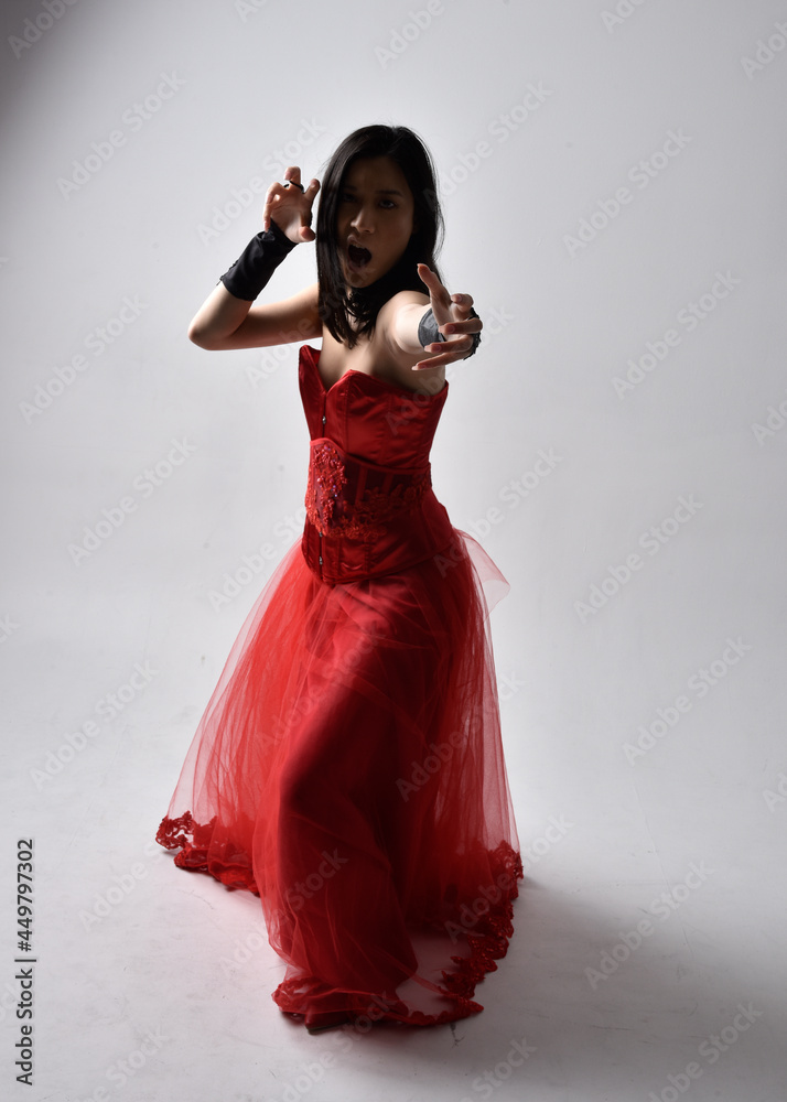 Wall mural Full length  portrait of beautiful young asian woman wearing red corset and ornate gothic queen crown. Graceful standing posing  isolated on studio background. - Wall murals