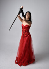 Full length  portrait of beautiful young asian woman wearing red corset and ornate gothic queen crown. Graceful standing posing  isolated on studio background.