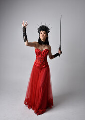 Full length  portrait of beautiful young asian woman wearing red corset and ornate gothic queen crown. Graceful standing posing  isolated on studio background.