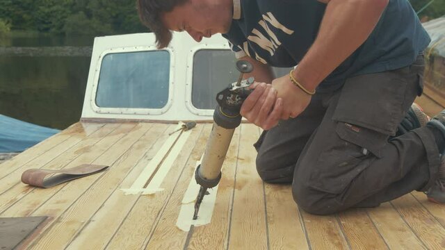 A young man applying sealant between wooden boat roof planks