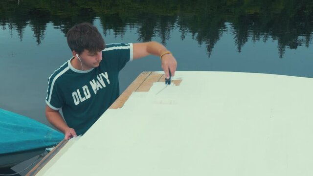 Young man finishes applying primer to wooden boat roof planks