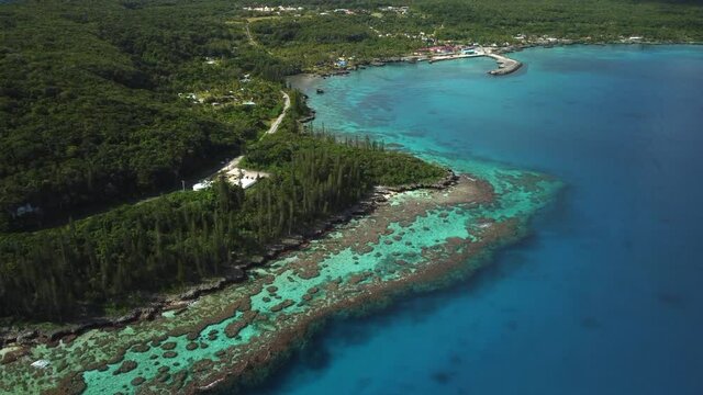 Aerial ascending shot revealing amazing coral bay beach and Tadine wharf, on Maré Island, New Caledonia