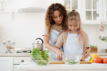 Mother and teen daughter preparing vegetable salad at kitchen