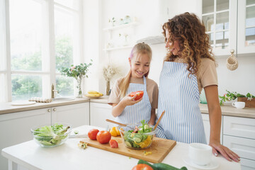 Mommy teaching her teen daughter to cook vegetable salad in kitchen