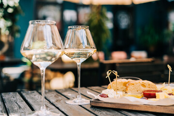 A wooden table in a restaurant with a cheese plate, grape, honey bread and white wine. Wine glasses and cheese served for a party in a blurred bar or a restaurant on terrace at a sunny summer day.