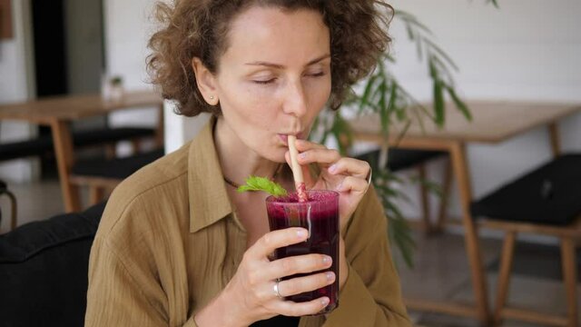 A young Caucasian woman enjoys her healthy organic cold pressed beetroot juice. Sipping it through the paper straw in a tropical cafe