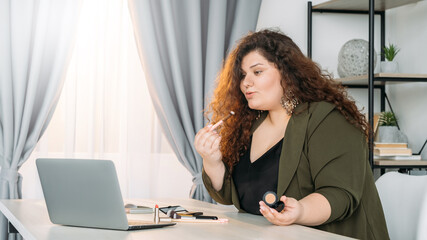 Beauty expert. Curvy female blogger. Decorative cosmetic. Advertising product. Smiling plus size woman demonstrating makeup tricks looking laptop table in light room interior copy space.