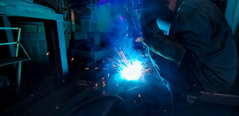 Welder welding metal with argon arc welding machine and has welding sparks. A man wears welding mask and protective gloves. Safety in industrial workplace. Welder working with safety. Steel industry.