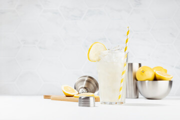 Fototapeta na wymiar Cooking lemon juice in soft light fresh elegant white kitchen in sunny day - lemonade in misted glass with straw, ice cubes with ingredients, silver bowl, shaker.