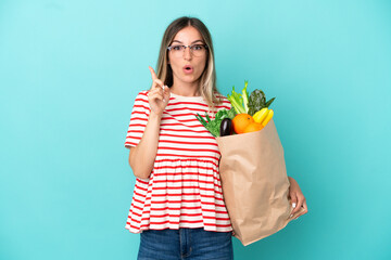 Young woman holding a grocery shopping bag isolated on blue background intending to realizes the solution while lifting a finger up