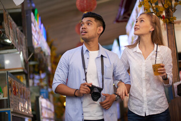 Multi-ethnic young couple walking along the street in city they traveled to and taking photos