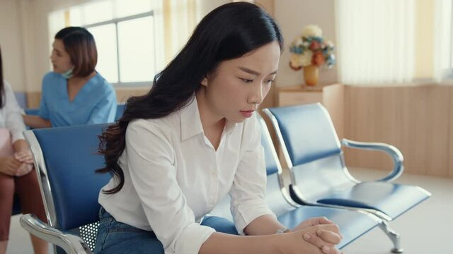Young Asian girl sitting on chair waiting room feel scary for bad news stress hopeless and sadness for her father in front surgical room at hospital, Hospital environment concept.
