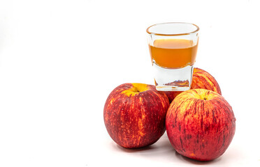 Small Shot Glass of organic Apple Cider Vinegar with the mother, raw and unpasteurized. Small Shot Glass of organic Apple Cider Vinegar is on three fresh apples on white background.
