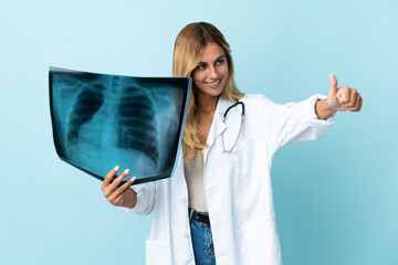 Young blonde Uruguayan doctor woman isolated on blue background giving a thumbs up gesture