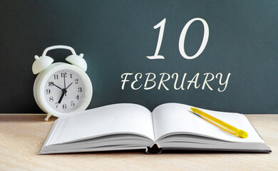 february 10. 10-th day of the month, calendar date.A white alarm clock, an open notebook with blank pages, and a yellow pencil lie on the table.Winter month, day of the year concept