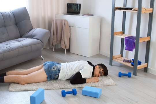 Funny nerd man in glasses is falling on carpet and sleeping on floor after fitness exercises at home. Training workout sport humor freak comic concept. Newcomer, beginner in sport. Tired man relaxing.