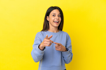 Young caucasian woman isolated on yellow background surprised and pointing front