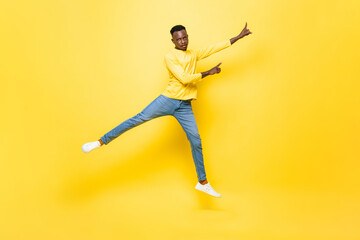 Fototapeta na wymiar Young energetic African man jumping and pointing hands up on isolated yellow studio background