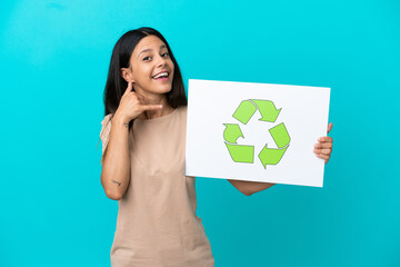 Young woman over isolated background holding a placard with recycle icon and doing phone gesture