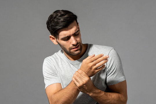 Young Caucasian man having wrist pain, studio shot in isolated gray background