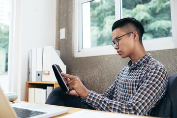 Serious businessman working at office table, he is reading document or using application on tablet computer