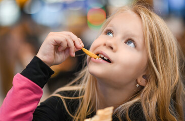 Little girl eating french fries in fast food cafe