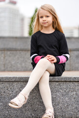 Little girl in a black dress sits on a bench