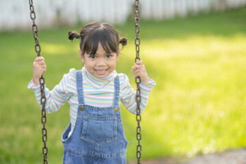 Happy little Asian girl playing swing outdoor in the park