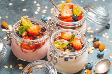 Yogurt with granola, fresh berries and nuts in a jar on a dark background. Healthy breakfast and dessert concept. Beautiful bright food photo