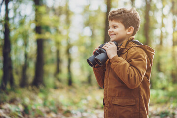 Portrait of boy who is hiking in nature with binoculars in autumn.