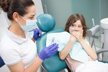 Scared young boy refusing to open his mouth for dental examination at the clinic