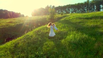 happy family is spinning in field. Mom and daughter turn, twist and laughing. Smile girl. drone flies away over hills. Aerial shot fly woman in white dress. run in green grass in summer sunny day. 