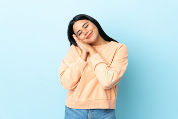 Young latin woman woman isolated on blue background making sleep gesture in dorable expression