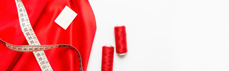Sewing accessories concept. Hobby sewing with thread, tape measure, red satin fabric. White...