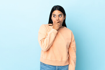 Young latin woman woman isolated on blue background doing surprise gesture while looking to the side