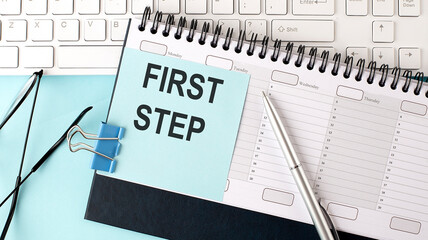 FIRST STEP text on blue sticker on the planning and keyboard,blue background